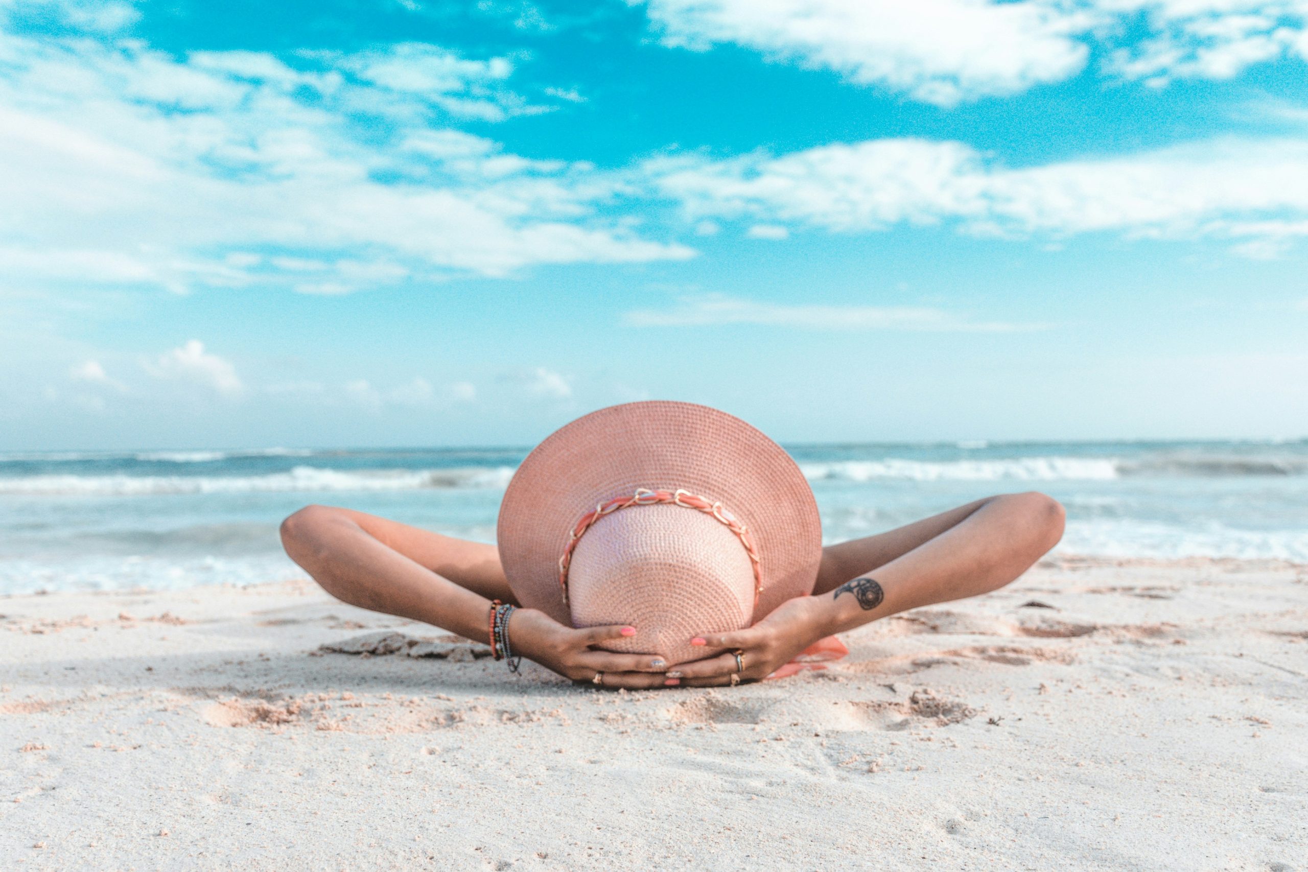 vacationer lying on a beach with a sun hat on