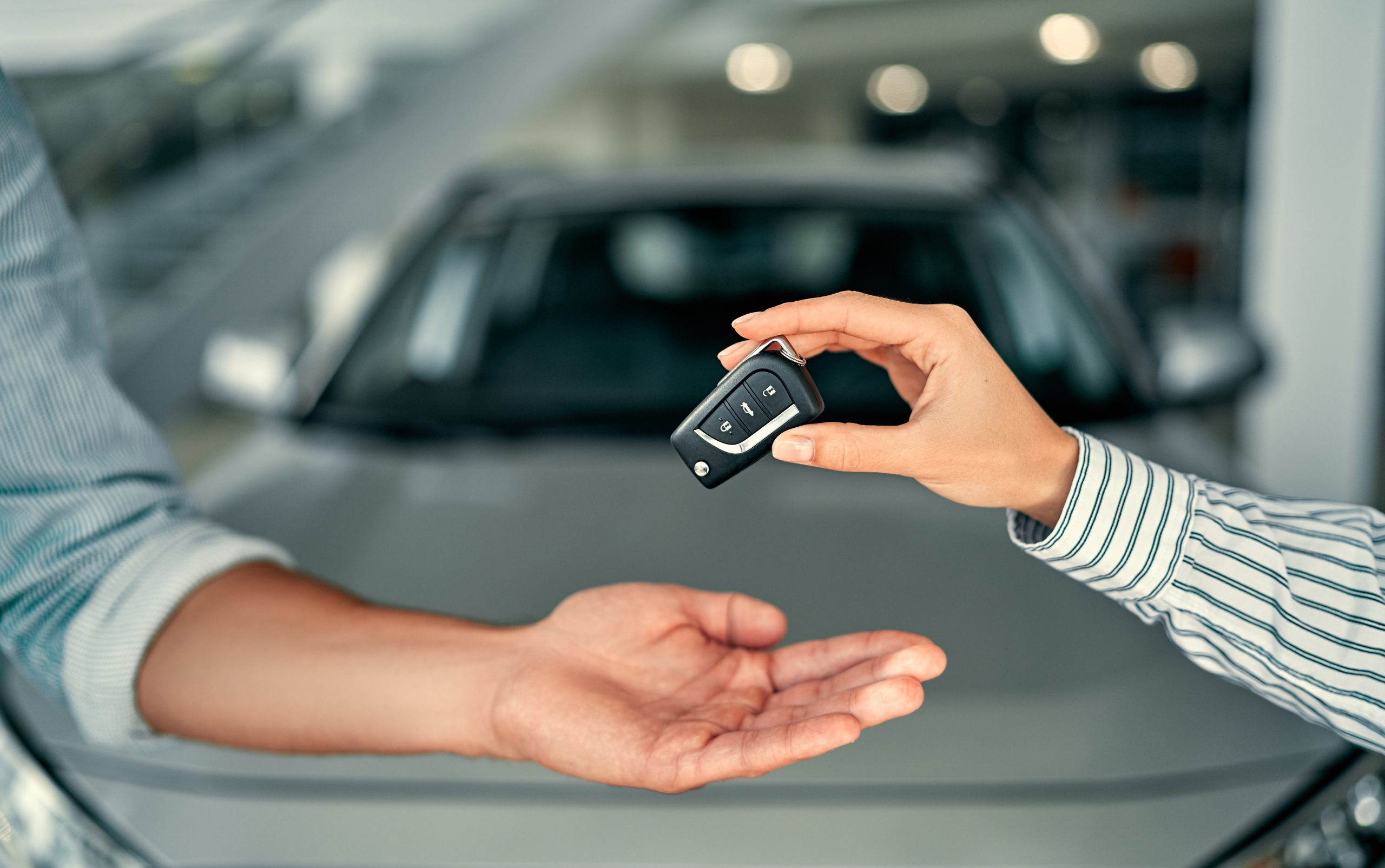 two people exchanging car keys in front of a car